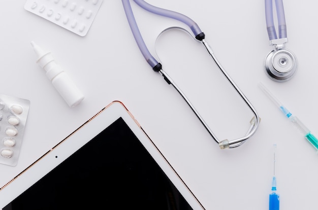 Digital tablet; pills; stethoscope and syringe on white backdrop