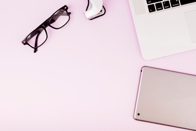 Digital tablet; spectacles and laptop on pink background