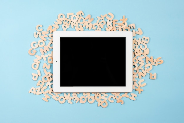 Digital tablet with black display screen on multiple wooden letters against blue background