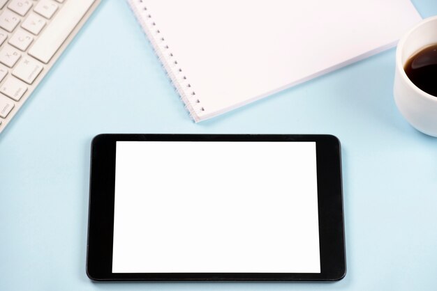 키보드가있는 디지털 태블릿; 파란색 배경에 나선형 메모장 및 커피 컵