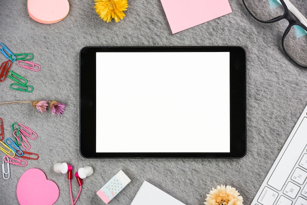 Бесплатное фото Цифровой планшет с белым экраном в окружении офисных принадлежностей на сером фоне