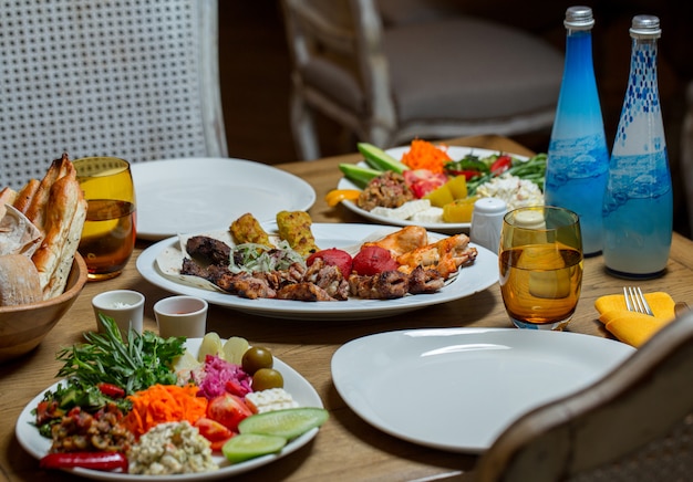 Dining table donated with variety of foods and two blue bottles of mineral water.