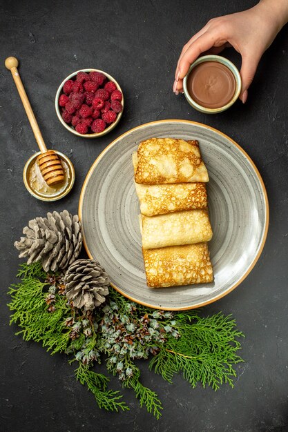 Dinner background with delicious pancakes honey and chocolate raspberry and conifer cone on black table