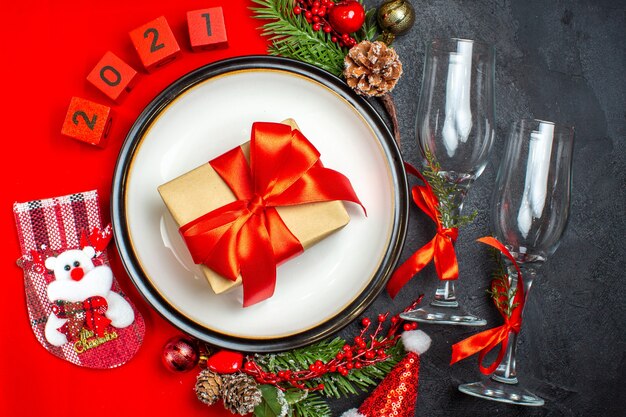 Обеденные тарелки украшения аксессуары еловые ветки рождественские носки цифры на красной салфетке и стеклянные бокалы на темном фоне