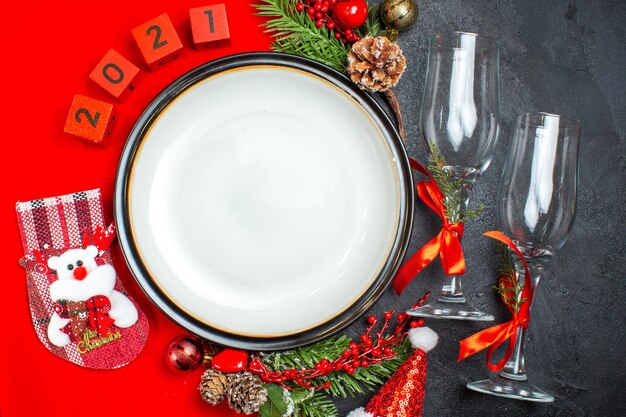Обеденные тарелки украшения аксессуары еловые ветки рождественские носки цифры на красной салфетке и стеклянные бокалы на темном столе