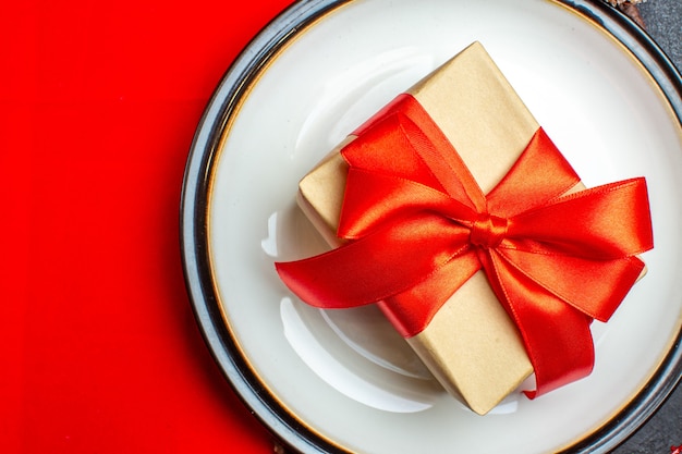 Dinner plates with bow-shaped gift with ribbon on a red napkin on a dark background