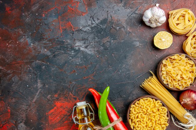 Dinner preparation with uncooked pastas cayenne peppers tied in one another with rope oil bottle lemon garlic on mixed color table