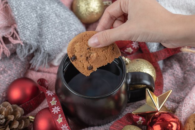 Dipping ginger cookie into drink on the table covered with christmas ornaments