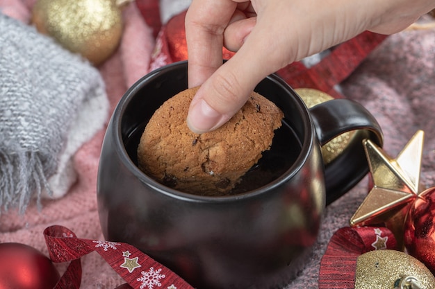 Dipping ginger cookie into drink on the table covered with christmas ornaments