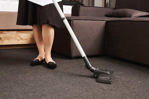 Free photo dirt have no chances to survive. cropped portrait of woman in maid uniform cleaning floor with vacuum cleaner, working in house of her employer, wiping all dirt and mess they left after party