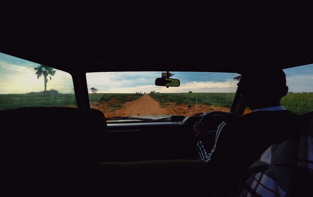 Dirt road in the middle of grassy fields shot from a car with a male driving