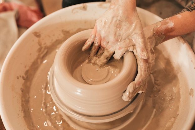 Free photo dirty female potter's hand modeling clay on a potter's wheel