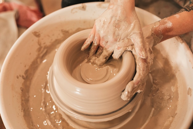 Грязная женская рука гончара лепит глину на гончарном круге