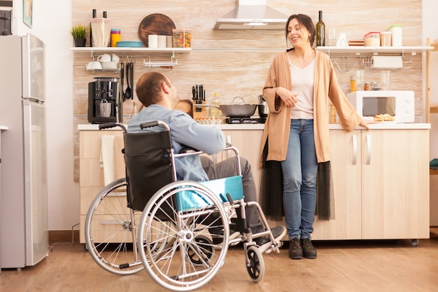 Disabled man sitting in chair and talking with wife while preparing meal. Disabled paralyzed handicapped man with walking disability integrating after an accident.