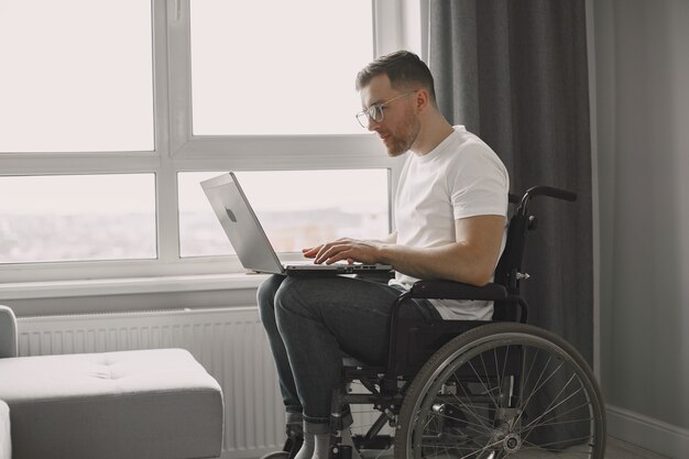Человек-инвалид с помощью ноутбука. Веселый красавец сидит дома и работает удаленно.