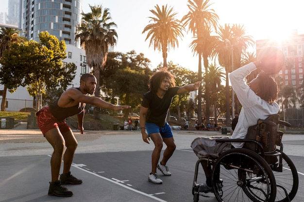 Free photo disabled man in wheelchair playing basketball with his friends outdoors