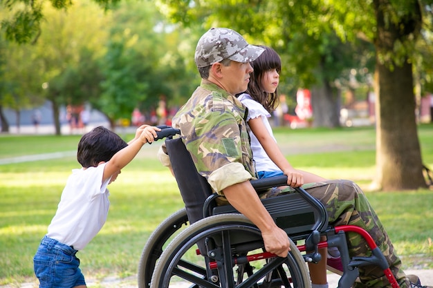 공원에서 두 아이 함께 걷는 장애인 군사 베테랑. 아빠 무릎, 휠체어를 밀고 소년에 앉아 소녀. 참전 용사 또는 장애 개념