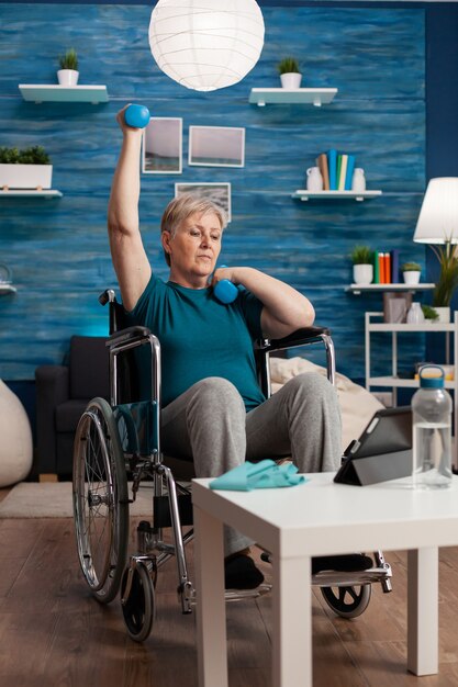 Disabled old woman in wheelchair raising arm training muscles resistance using dumbbells