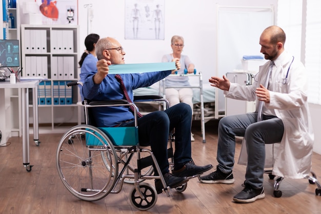 Старший мужчина-инвалид делает упражнения в больнице с врачом