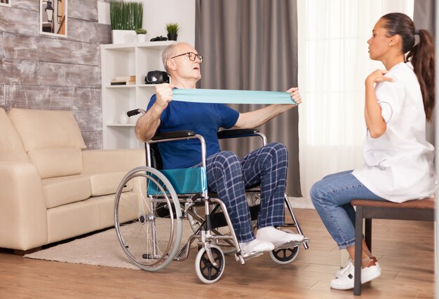 Disabled senior patient working out at home with resistance band under the guidance of a nurse