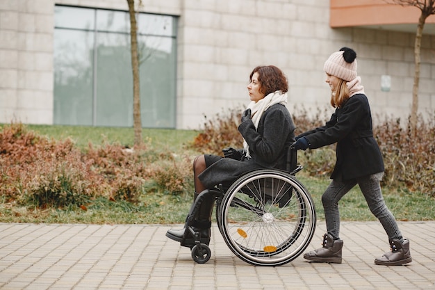 무료 사진 딸과 함께 휠체어에 장애인 여자입니다. 공원에서 밖에 걷는 가족.