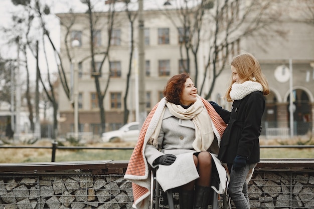 娘と車椅子の障害のある女性。公園で外を歩いている家族。少女は母親を格子縞で覆った。