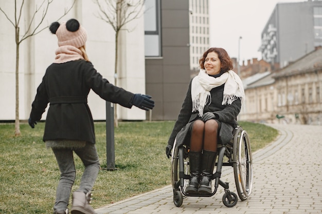 Женщина-инвалид в инвалидной коляске с дочерью. Семья гуляет в парке.
