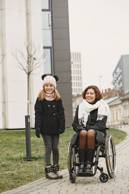 Disabled woman in wheelchair with daughter. Family walking outside at park.