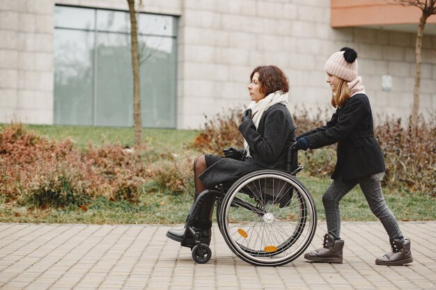 딸과 함께 휠체어에 장애인 여자입니다. 공원에서 밖에 걷는 가족.