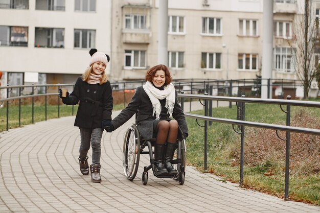 娘と車椅子の障害のある女性。公園で外を歩いている家族。