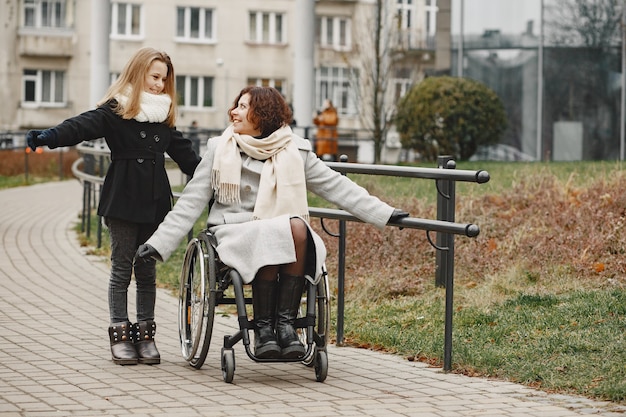 娘と車椅子の障害のある女性。公園で外を歩いている家族。