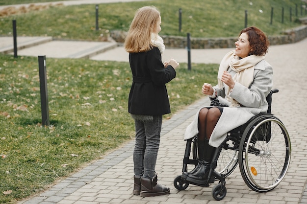 娘と車椅子の障害のある女性。公園で外を歩いている家族。