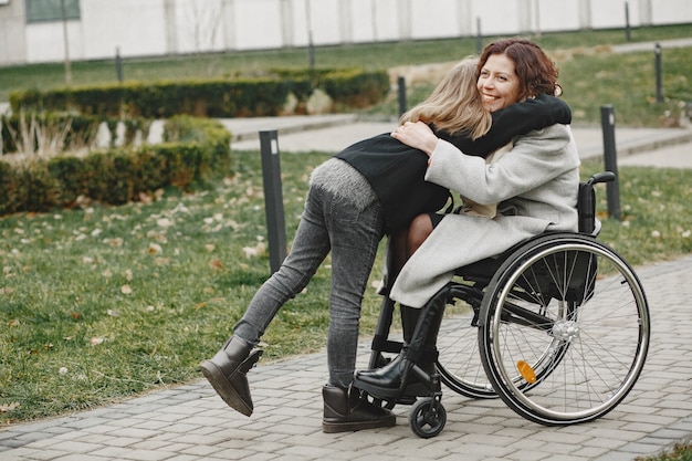 딸과 함께 휠체어에 장애인 여자입니다. 공원에서 밖에 걷는 가족.