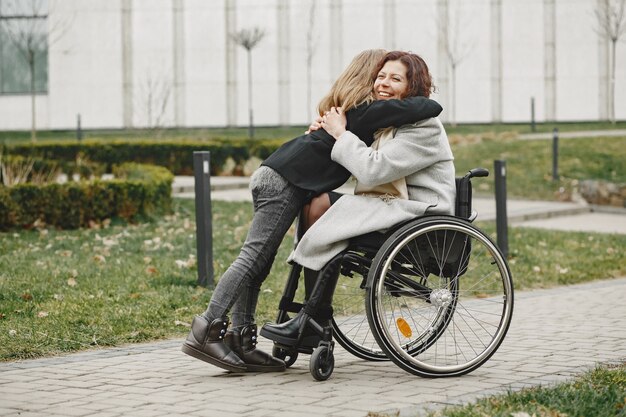 Disabled woman in wheelchair with daughter. Family walking outside at park.