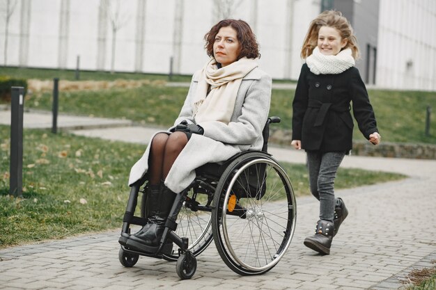 Disabled woman in wheelchair with daughter. Family walking outside at park.