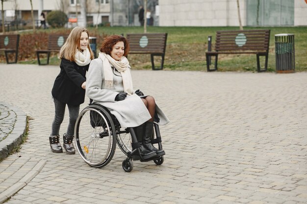 娘と車椅子の障害のある女性。公園で外を歩いている家族。