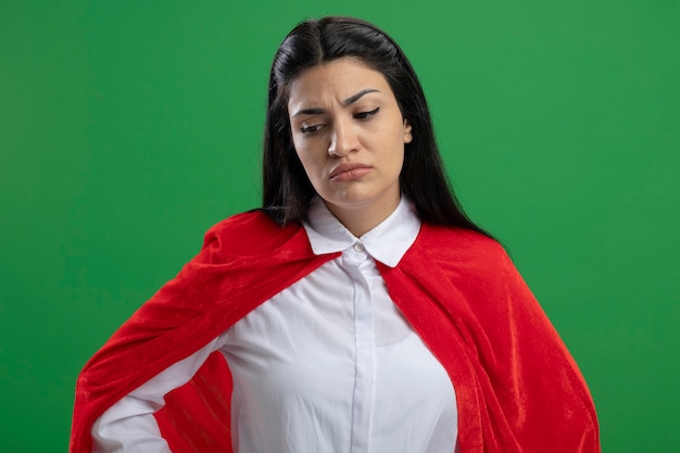 Foto gratuita disaffettata giovane superdonna tenendo la mano sui fianchi con la faccia dispiaciuta guardando in basso isolato sulla parete verde