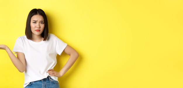 Free photo disappointed asian woman asking so what raise hand up and staring skeptical at camera standing over