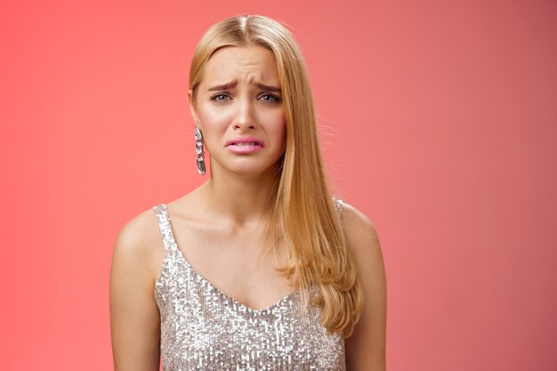 Disappointed complaining cute blond woman in silver stylish dress grimacing frowning upset have bad day pouting pity standing displeased unhappy heartbroken everything bad, red background