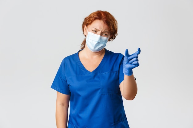 실망하고 불평하는 여성 의사, 간호사 또는 의사가 너무 작은 것을 보여주고 불쾌 해 보이며 안면 마스크와 장갑을 착용하십시오.
