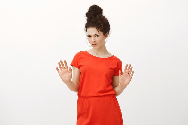 Disappointed doubtful attractive female coworker in stylish red dress, raising palms in no or stop gesture