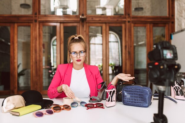 Disappointed girl in glasses and pink jacket sadly looking in camera while recording new fashion video for vlog