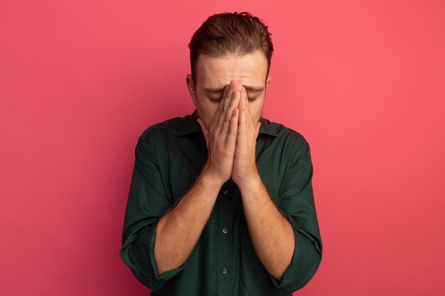 Disappointed handsome blonde man puts hands on face isolated on pink wall