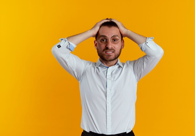 Disappointed handsome man with optical glasses holds head isolated on orange wall