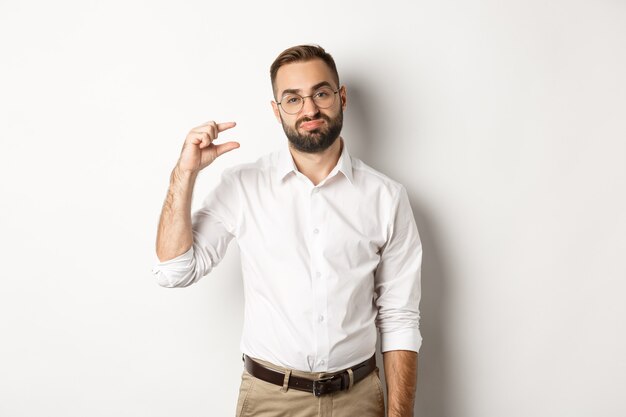 Disappointed male entrepreneur showing small object and sighing, standing  