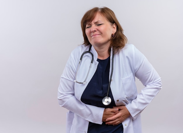 Foto gratuita medico donna di mezza età deluso che indossa veste medica e stetoscopio mani sui reni che soffrono di dolore ai reni sul muro bianco isolato con lo spazio della copia