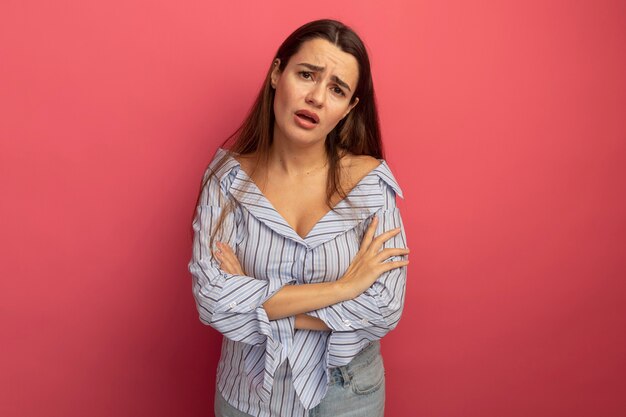 Disappointed pretty caucasian woman stands with crossed arms on pink