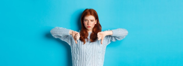 無料写真 悪い製品を判断する親指を示すセーターに失望した赤毛の女の子は同意せず、プロを嫌います