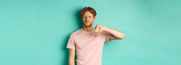 Free photo disappointed redhead man showing thumbsdown frowning and looking skeptical epxress dislike and disap