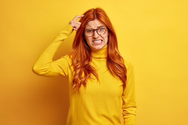 がっかりした赤毛の若い女性は、頭を引っかいて歯を食いしばってカジュアルなタートルネックを着ているのではないかと疑っています。